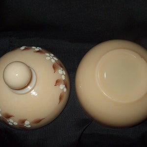 May include: A vintage glass candy dish with a lid. The dish is a pale peach color with a brown and white floral design. The lid has a knob on top.