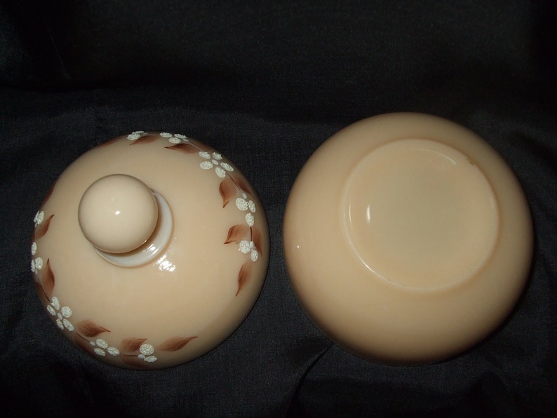 May include: A vintage glass candy dish with a lid. The dish is a pale peach color with a brown and white floral design. The lid has a knob on top.