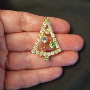 May include: A gold-tone Christmas tree pin with clear, green, pink, and purple rhinestones.