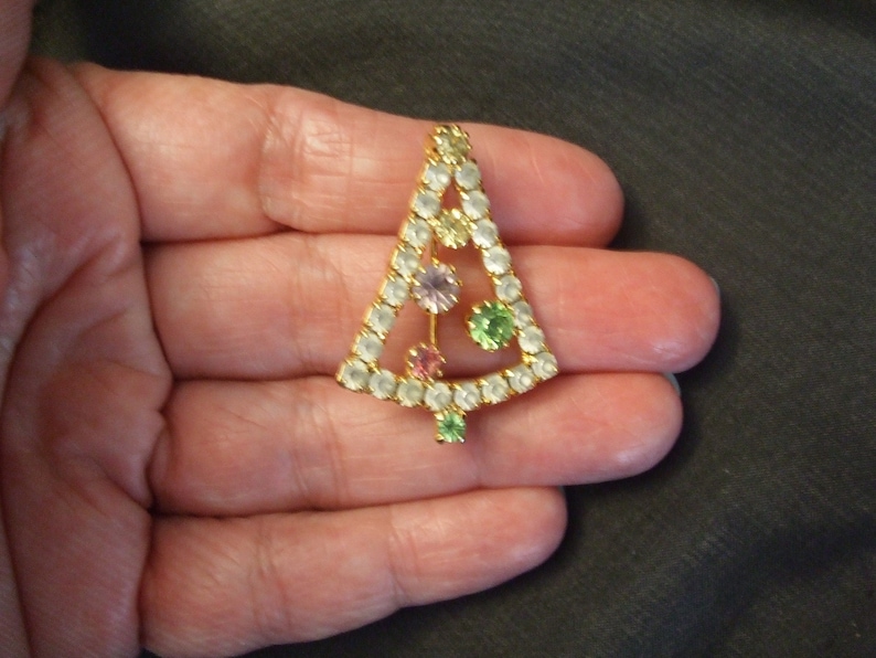 May include: A gold-tone Christmas tree pin with clear, green, pink, and purple rhinestones.