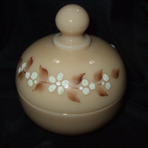 May include: A vintage glass jar with a lid, featuring a floral design in brown and white. The jar is a pale peach color.
