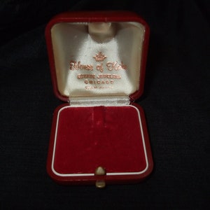 May include: Open red jewelry box with a white interior and gold lettering that reads "House of Kahn, Estate Jewelers, Chicago". The box has a red velvet interior and a gold clasp.
