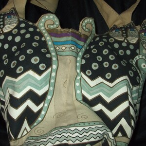May include: A beige tote bag with a black, white, and green cat design. The cats have a geometric pattern with circles, zigzags, and swirls.