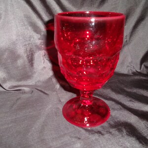 May include: A ruby red goblet with a textured, faceted design. The stem and base are also red, and the glass has a sparkling appearance. The goblet is likely made of glass and is suitable for serving beverages.