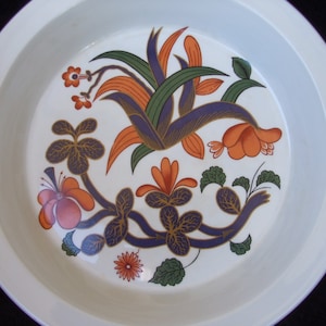 May include: A white ceramic pie plate with a floral design featuring orange, purple, green, and gold accents. The design includes stylized flowers and leaves.