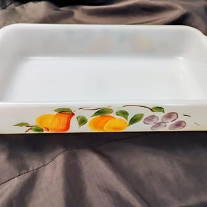 May include: White rectangular baking dish with handles. The dish is decorated with a hand-painted design of yellow and orange fruit with green leaves and purple grapes. The dish is empty.