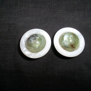 May include: Two white, round, decorative objects with a green and white marble design inside.