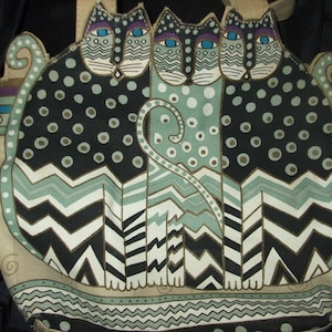 May include: A beige tote bag with a black, white, and green pattern of three stylized cats. The bag has a brown leather handle and a label that reads "Susan Branch".