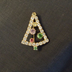 May include: A gold-tone Christmas tree brooch with clear, green, and purple rhinestones.