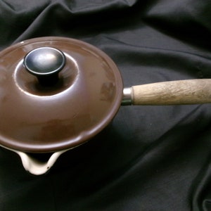 May include: A brown enameled cast iron saucepan with a wooden handle and a lid. The lid has a black knob.