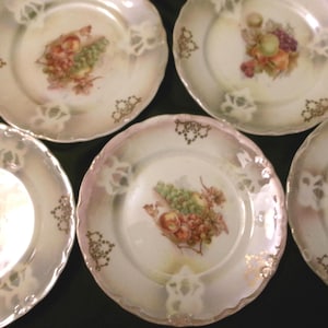 May include: Five white porcelain plates with gold trim and a fruit design. Each plate features a different arrangement of grapes, apples, and berries.