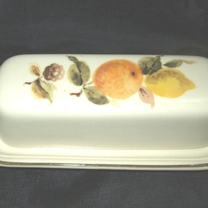 May include: A white ceramic butter dish with a gold trim. The dish features a painted design of lemons and oranges with green leaves.