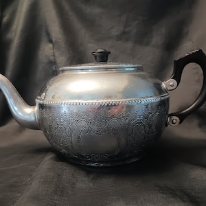 May include: A silver teapot with an ornate floral design and a black handle. The teapot has a shiny finish and a classic design.