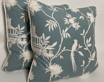 May include: Two square decorative pillows with a teal background and a white floral and bird pattern. The pillows have white piping around the edges. The design includes flowers, branches, and a bird.