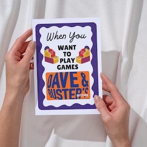 May include: A white card with a purple border and the text "When You Want To Play Games." The card features illustrations of arcade game machines and the "Dave & Buster's Gift Card" logo in orange.