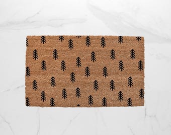 May include: A rectangular doormat with a natural brown coir fiber surface. The mat features a repeating pattern of black stylized fir trees. The doormat is designed for outdoor use and measures approximately 30 inches long.