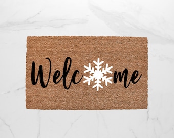 May include: A brown coir doormat with the word "Welcome" in black cursive lettering and a white snowflake in the center.