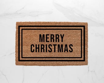 May include: A rectangular doormat made of natural brown coir fiber. The mat features a black border and the words "MERRY CHRISTMAS" in bold, black capital letters, perfect for holiday decor.