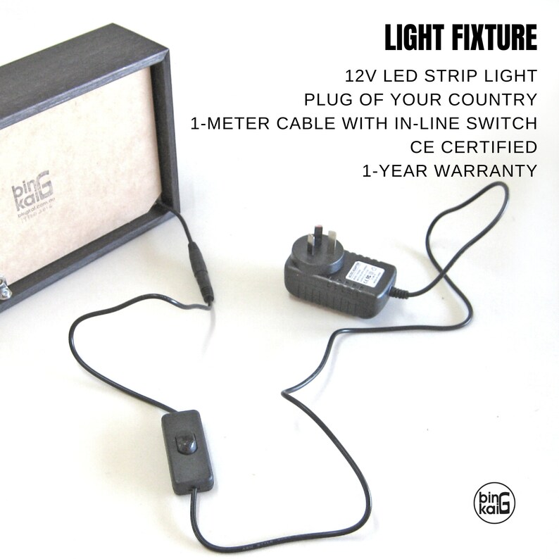 Pode incluir: Uma moldura de madeira preta com um adaptador de energia preto, um interruptor em linha preto e um cabo preto. A moldura tem um r&oacute;tulo branco com o texto "bing kali" nele. O texto "LIGHT FIXTURE" est&aacute; escrito em preto acima do texto "12V LED STRIP LIGHT". O texto "PLUG OF YOUR COUNTRY" est&aacute; escrito abaixo do texto "12V LED STRIP LIGHT". O texto "1-METER CABLE WITH IN-LINE SWITCH" est&aacute; escrito abaixo do texto "PLUG OF YOUR COUNTRY". O texto "CE CERTIFIED" est&aacute; escrito abaixo do texto "1-METER CABLE WITH IN-LINE SWITCH". O texto "1-YEAR WARRANTY" est&aacute; escrito abaixo do texto "CE CERTIFIED".