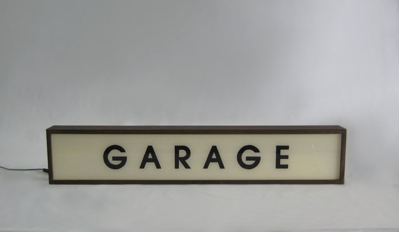 Pode incluir: Uma placa retangular marrom com fundo branco e letras pretas que diz "GARAGE".