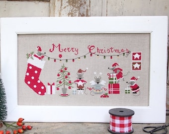 Könnte beinhalten: Eine Kreuzstich-Stickerei in einem weißen Rahmen mit beigefarbenem Hintergrund. Die Stickerei zeigt eine Weihnachtsszene mit einem Strumpf, einem Weihnachtsbaum und mehreren Mäusen, die Geschenke halten. Der Text "Merry Christmas" ist in Rot über der Szene gestickt.