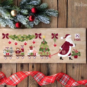 Peut inclure: Un motif de point de croix rectangulaire sur tissu beige représentant un Père Noël tirant un train de petits chariots chargés de jouets et un sapin de Noël. Le design inclut des nœuds rouges, des décorations suspendues et le texte "X mas" en rouge.
