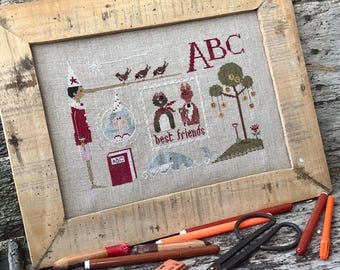 Puede incluir: Un diseño de punto de cruz enmarcado que presenta una ilustración caprichosa de niños jugando con el texto "ABC best friends". El marco está hecho de madera natural con un acabado rústico.