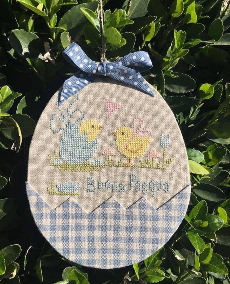 May include: A blue and white gingham fabric egg-shaped ornament with a cross-stitch design of two yellow chicks and the text "Happy Easter".