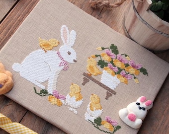 May include: A cross-stitch design featuring a white rabbit with a pink collar and a yellow chick on its back. The design includes yellow chicks hatching from eggs and a floral arrangement. The image also includes decorative bunny and chick shaped candies.