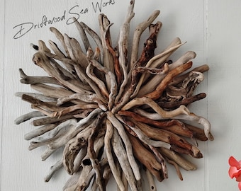 May include: A circular wall art piece composed of numerous pieces of weathered driftwood arranged in a sunburst pattern. The wood varies in color from light gray to deep brown. The text Driftwood Sea Works is visible above the object.