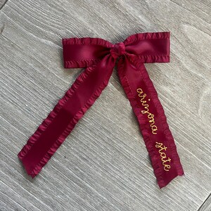 May include: A burgundy satin ribbon bow with a gold embroidered inscription that reads "original state".