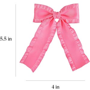 May include: A pink satin bow with ruffled edges. The bow measures 5.5 inches in length and 4 inches in width.