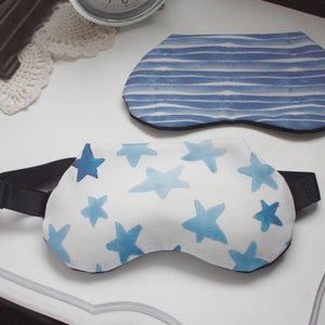 Puede incluir: Dos antifaces para dormir con patrones azules y blancos. Un antifaz tiene un patr&oacute;n de rayas azules y blancas, y el otro tiene un fondo blanco con estrellas azules. Ambos antifaces tienen cintas el&aacute;sticas negras.