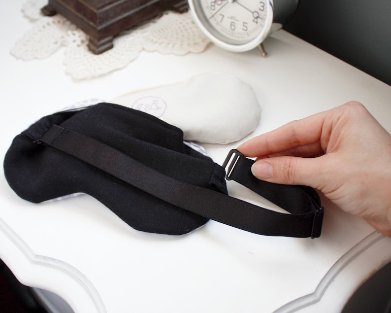May include: Black sleep mask with an adjustable strap and a black buckle. The mask is made of a soft, comfortable fabric.