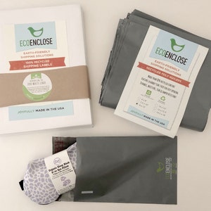 K&ouml;nnte beinhalten: Ein Stapel wei&szlig;er Umschl&auml;ge mit einem braunen Etikett mit der Aufschrift "ECOENCLOSE Umweltfreundliche Versandl&ouml;sungen 100 % recycelte Versandetiketten" und einem gr&uuml;n-wei&szlig;en Aufkleber mit der Aufschrift "Einf&uuml;hrung des Zero Waste Liners" sowie ein Stapel grauer Poly-Versandtaschen mit einem Etikett mit der Aufschrift "ECOENCLOSE Umweltfreundliche Versandl&ouml;sungen Recycelte Poly-Versandtaschen Hergestellt aus 100 % recyceltem Inhalt Mit einem robusten Verschluss f&uuml;r einfaches &Ouml;ffnen Strapazierf&auml;hig, feuchtigkeitsbest&auml;ndig, rei&szlig;fest und manipulationssicher" und eine graue Poly-Versandtasche mit einer lila-wei&szlig;en Augenmaske im Inneren.