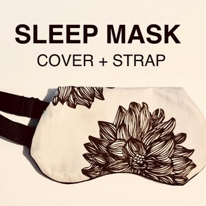 May include: Sleep mask with a floral design. The sleep mask is white with a large brown floral pattern and a black strap. The text "SLEEP MASK COVER + STRAP" is above the mask.