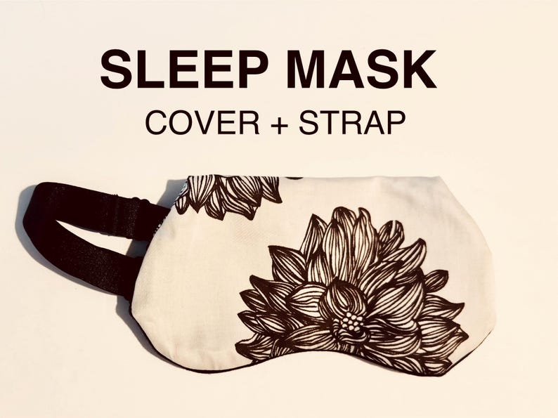 May include: Sleep mask with a floral design. The sleep mask is white with a large brown floral pattern and a black strap. The text "SLEEP MASK COVER + STRAP" is above the mask.
