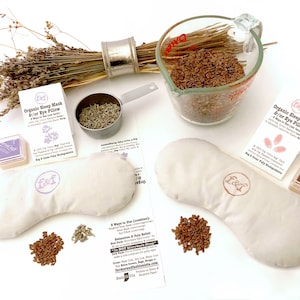 May include: A DIY kit for making a lavender and flax seed eye pillow. The kit includes two white fabric eye pillows, a bag of flax seeds, a bag of dried lavender, a small measuring cup, two ink pads, and two stamps. The kit comes with instructions on how to make the eye pillow.