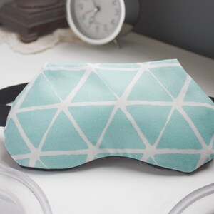 May include: A light blue sleep mask with a white geometric pattern. The mask has an adjustable black elastic strap.