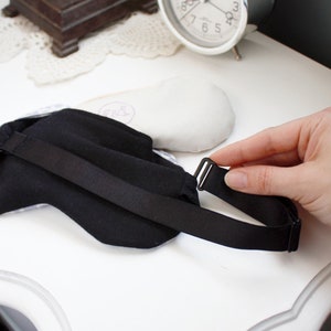 May include: Black sleep mask with an adjustable strap and a black buckle. The mask is made of a soft, comfortable fabric.
