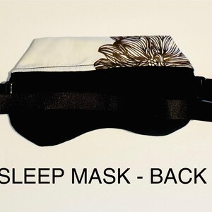 May include: Black sleep mask with an adjustable strap. The top section features a white fabric with a brown floral pattern. The text "SLEEP MASK - BACK" is printed in black at the bottom of the image.