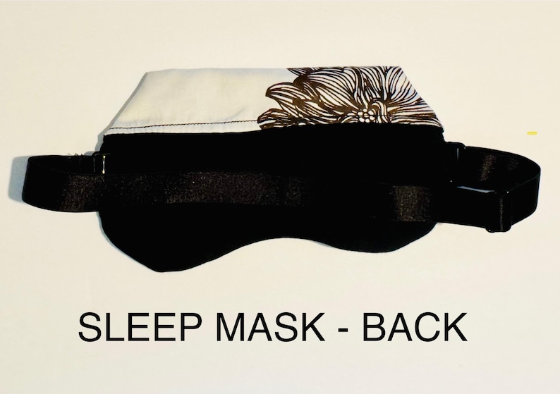 May include: Black sleep mask with an adjustable strap. The top section features a white fabric with a brown floral pattern. The text "SLEEP MASK - BACK" is printed in black at the bottom of the image.