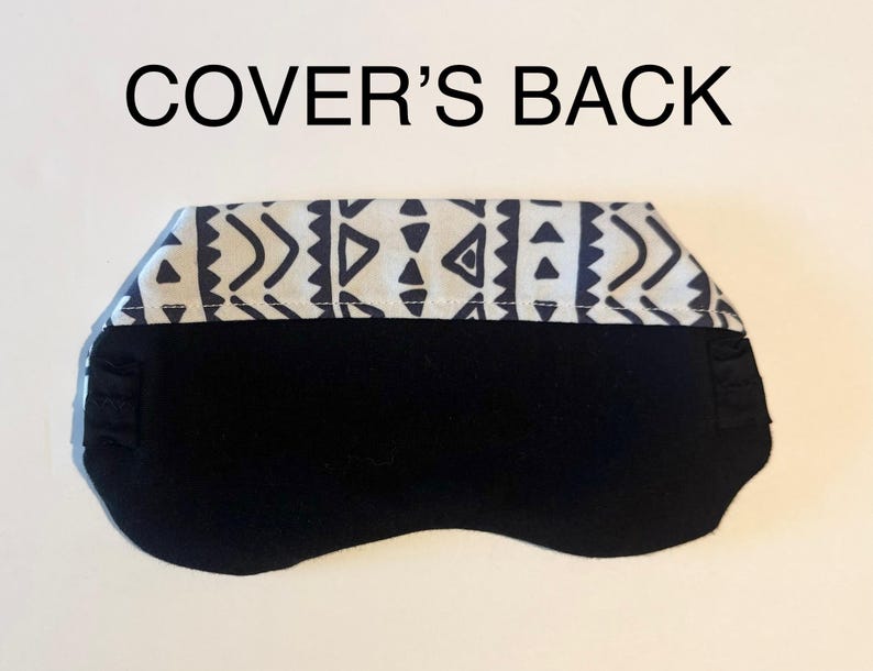 May include: Black sleep mask with a patterned top band. The top band features a white background with a repeating geometric design in navy blue. The text "COVER'S BACK" is above the mask.