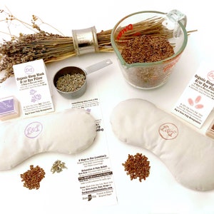May include: A DIY kit for making a lavender and flax seed eye pillow. The kit includes two white fabric eye pillows, a bag of flax seeds, a bag of dried lavender, a small measuring cup, two ink pads, and two stamps. The kit comes with instructions on how to make the eye pillow.
