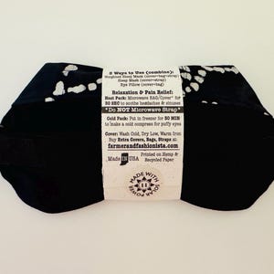 May include: Black sleep mask with white spotted pattern and an adjustable strap. The mask has a label with instructions for use, including microwave and cold pack options. Made in the USA.