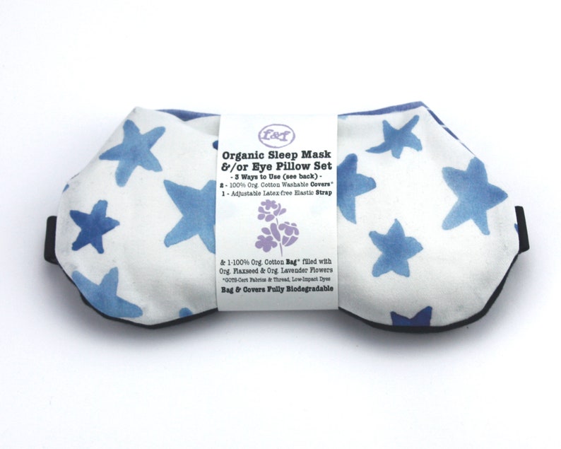 Puede incluir: Una m&aacute;scara para ojos blanca con un patr&oacute;n de estrellas azules y un borde negro. La m&aacute;scara est&aacute; hecha de algod&oacute;n org&aacute;nico y rellena de semillas de lino y lavanda. La etiqueta dice "Organic Sleep Mask &/or Eye Pillow Set - 3 Ways to Use (see back) - 100% Org. Cotton Washable Covers 1-Adjustable Latex free Elastic Strap & 1-100% Org. Cotton Bag" filled with Org. Flaxseed & Org Lavender Flowers 0016 Cert Paris & Thread, Low Impact Dyes Bag & Covers Fully Biodegradable"