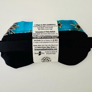 May include: A black eye mask with a turquoise and gold star pattern on the top. The mask has a black strap and a white label with text about its uses and care instructions. The product is made in the USA.