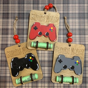 May include: Three wooden ornaments with a painted video game controller design. Each ornament has a slot to hold a rolled up bill of money. The ornaments are labeled "Gaming Money".