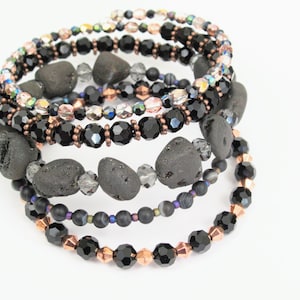 May include: A set of five black and copper beaded bracelets with black lava rock beads. The bracelets are stacked on top of each other.