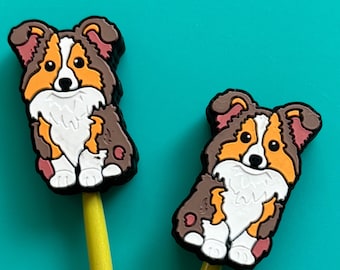 May include: Two yellow wooden pencils with brown and white cartoon dog toppers. The dogs are sitting up and have brown, white, and orange fur.